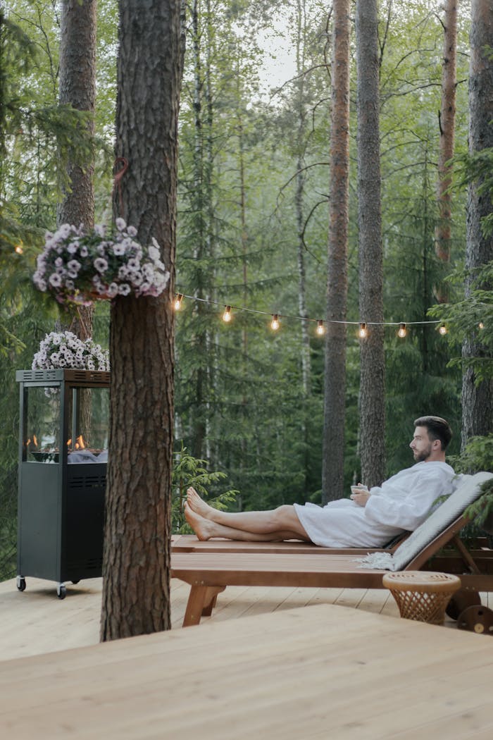 A man in a bathrobe enjoys a peaceful moment on a wooden deck surrounded by nature.