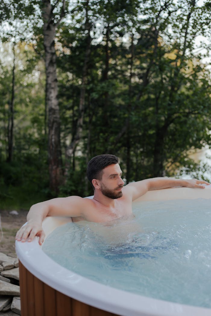 Shirtless man relaxing in a hot tub in nature, enjoying leisure time and wellness outdoors.