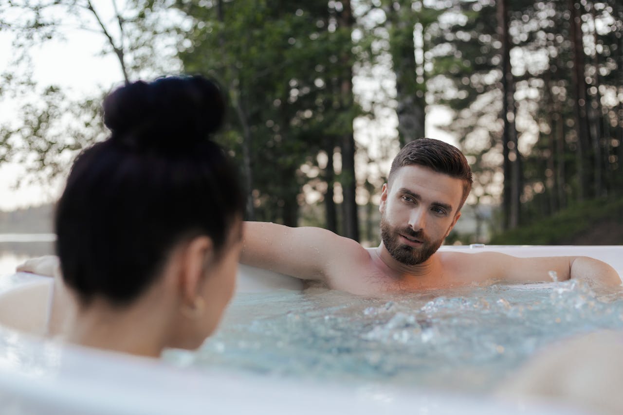 A couple enjoys a relaxing moment in an outdoor jacuzzi surrounded by trees, capturing a serene vacation vibe.